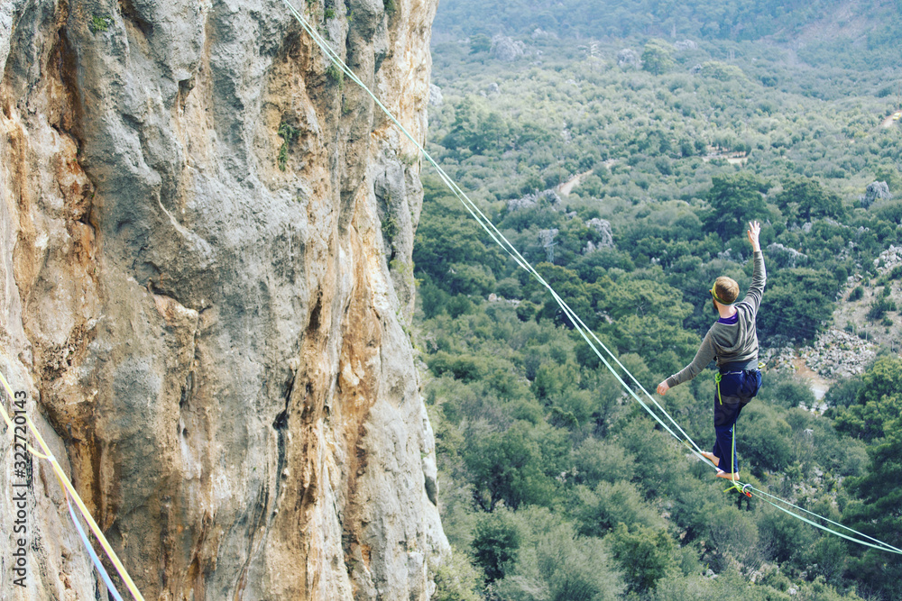 A man is walking along a stretched sling. Highline in the mountains. Man catches balance. Performance of a tightrope walker in nature. Highliner on the background of valley.