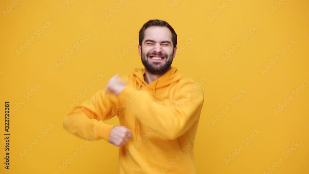 Handsome happy bearded young guy 20s in yellow streetwear hoodie isolated on yellow background studio. People lifestyle concept. Dancing fooling around having fun expressive gesticulating with hands Handsome happy bearded young guy 20s in yellow streetwear hoodie isolated on yellow background studio. People lifestyle concept. Dancing fooling around having fun expressive gesticulating with hands