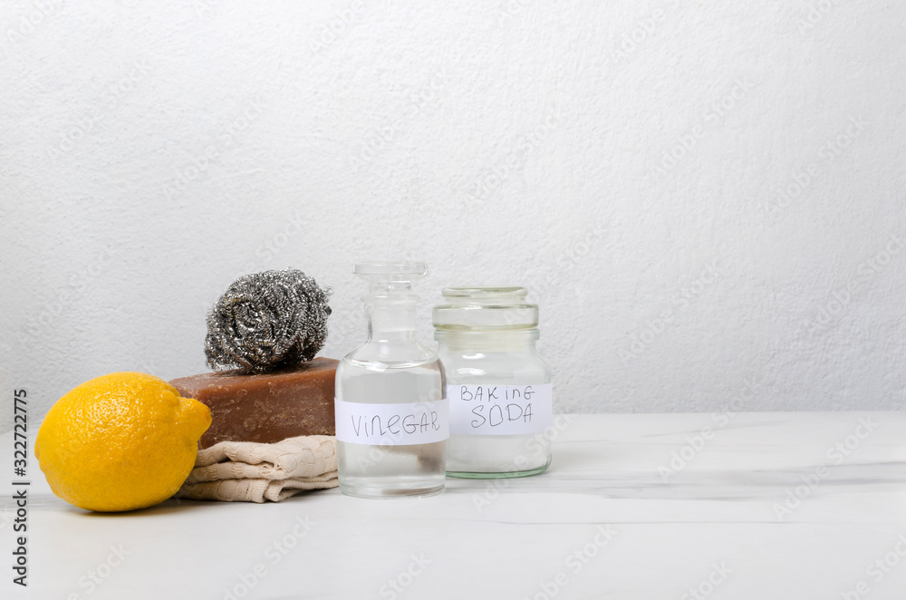 Lemon, soap, sponges, natural soap, glass jar of white vinegar and backing soda on the white kitchen table against white wall.Concept of eco friendly cleaning.Empty space for text Lemon, soap, sponges, natural soap, glass jar of white vinegar and backing soda on the white kitchen table against white wall.Concept of eco friendly cleaning.Empty space for text