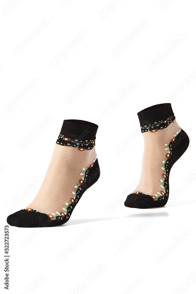 Cropped shot of female feet on tiptoe in flesh-colored nylon sheer socks with an embroidered floral pattern, black toes, bottoms and rims. The photo is made on the white background. Cropped shot of female feet on tiptoe in flesh-colored nylon sheer socks with an embroidered floral pattern, black toes, bottoms and rims. The photo is made on the white background.