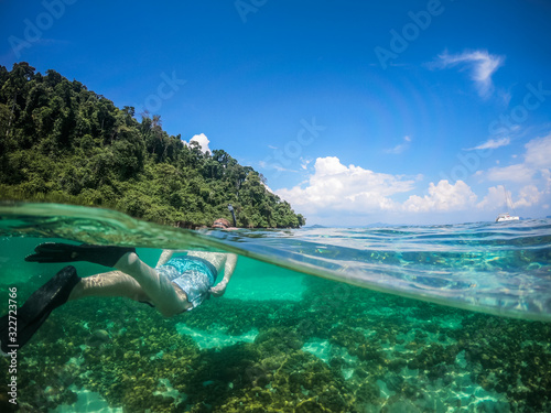 Over and Underwater Dome Shot of man snorkling in front of a private sailing yacht in Thailand over a coral reef
