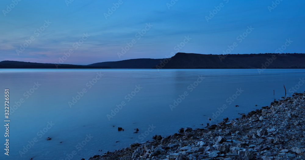 long exposure landscape night time lake calm water surface stone coast line and horizon background main land scenic view with blue toning style photography panoramic wallpaper concept