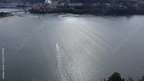 Aerial, tilt up, drone shot of a Jetski water scooter, heading towards a town, at the coast of Galcia, on a sunny day, in North Spain photo