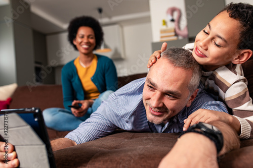 Smiling mixed race family enjoying time at home laying on sofa in living room making selfie with tablet.