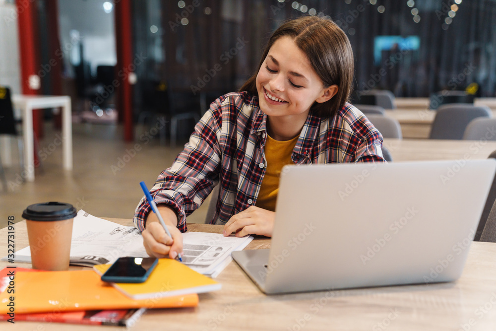 Image of smiling girl doing homework with laptop and exercise books Image of smiling girl doing homework with laptop and exercise books