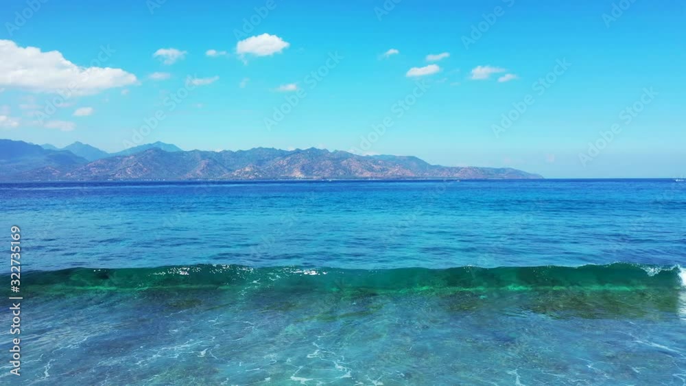 Beautiful view of a shallow wave breaking and crashing against the shore and scenic mountains and cloudy sky in the background Beautiful view of a shallow wave breaking and crashing against the shore and scenic mountains and cloudy sky in the background