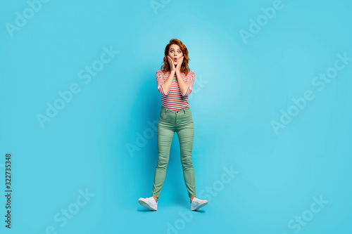 Full length photo of pretty lady arms on cheeks enjoy traveling abroad see historic building wear casual red white shirt green pants footwear isolated blue color background