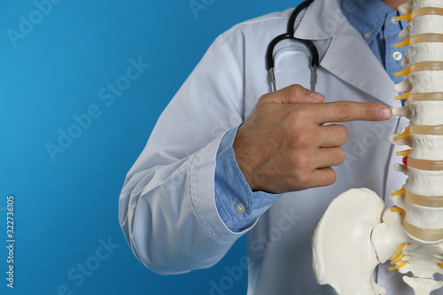 Male orthopedist with human spine model against blue background, closeup photo