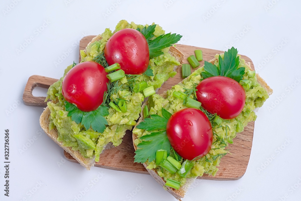 Black bread sandwiches with avocado, with red cherry tomatoes and herbs on a wooden cutting board. Close-up Black bread sandwiches with avocado, with red cherry tomatoes and herbs on a wooden cutting board. Close-up