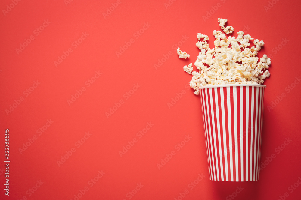 Overturned paper cup with delicious popcorn on red background, top view. Space for text