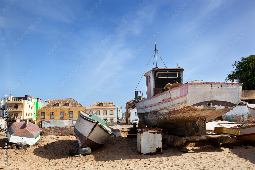 Old weathered boats parked on the beach of Sal Rei with colorful houses in the background on Boa Vista in Cape Verde
