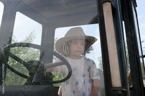 Fotografie Little girl in the cab of the tractor holds the wheel