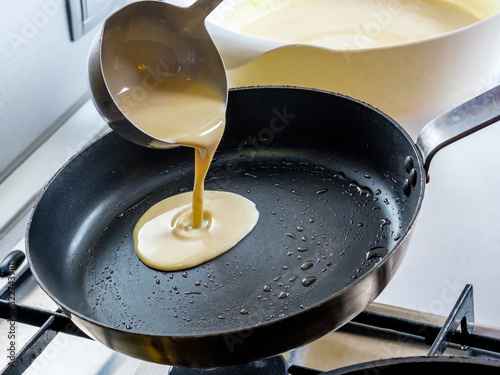 Batter pouring out of a metal bucket onto a red-hot greased frying pan. The process of baking pancakes. photo