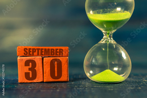 september 30th. Day 30 of month,Handmade wood cube with date month and day and hourglass with green sand. Time passing away. artistic coloring.  autumn month, day of the year concept