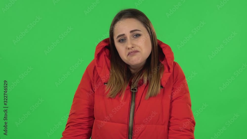 Portrait of lovely girl in a red down jacket upset and shrugging. Green screen