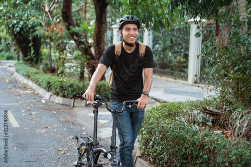 smiling asian young man walking with folding bike on the street