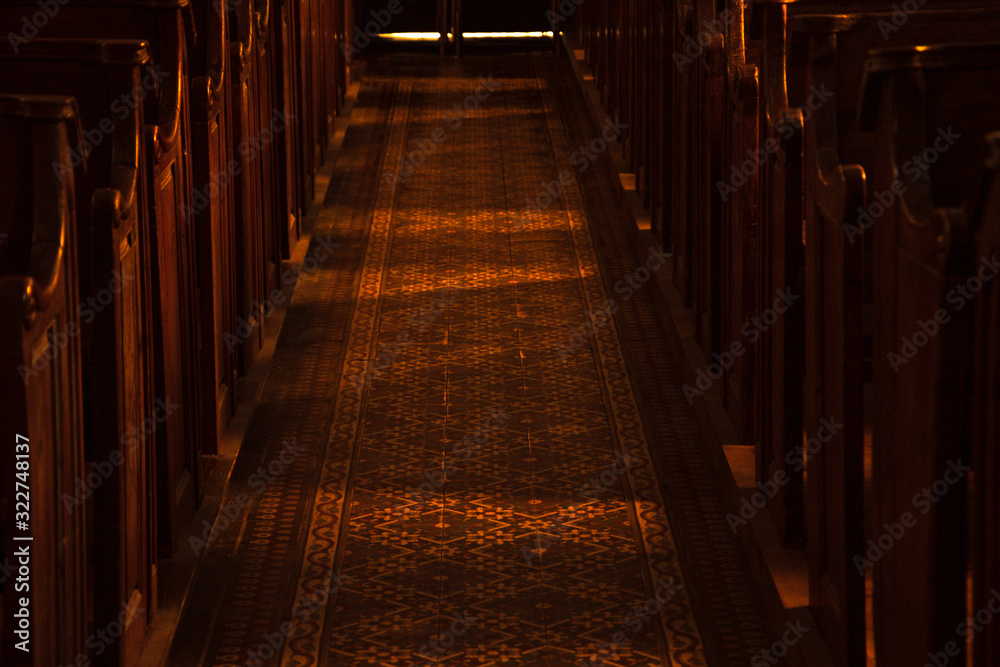 Temple mystery. Wooden benches in dark empty church. Sunlight lightens the pews and passage floor with beautiful pattern. Religious background. Divine light, grace, hope, miracle concepts.