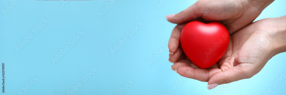 Woman hand hold red toy heart in hand against blue background closeup. Charity people concept Woman hand hold red toy heart in hand against blue background closeup. Charity people concept