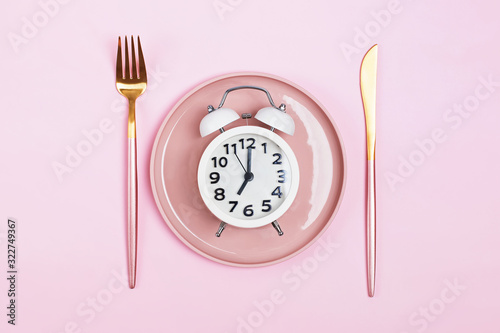 Retro alarm clock on plate with fork and knife isolated on pink background.
