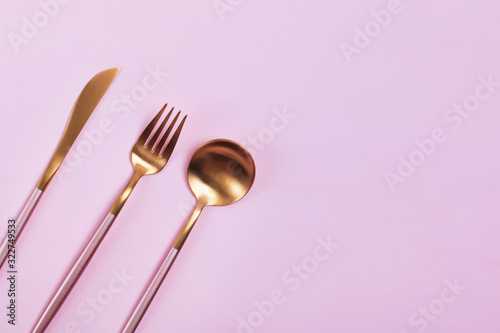 Elegant golden cutlery on pink background