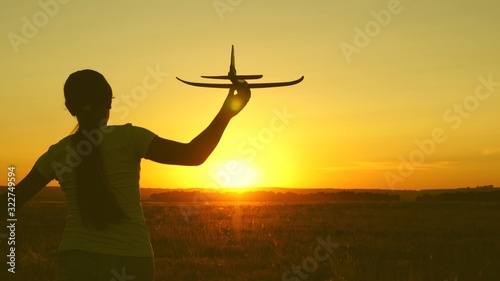 children play toy airplane. Happy girl runs with a toy airplane on a field in the sunset light. teenager dreams of flying and becoming pilot. the girl wants to become pilot and astronaut.