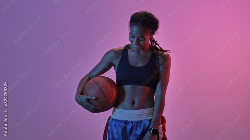 Cheerful african sports woman holding ball and rejoicing isolated led flashlights background Cheerful african sports woman holding ball and rejoicing isolated led flashlights background