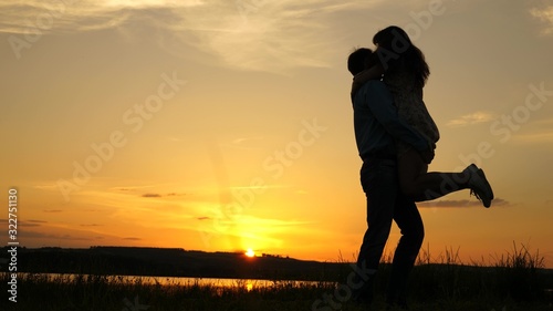 Fototapeta Naklejka Na Ścianę i Meble -  Young couple dancing at sunset on beach. Happy guy and girl waltz in evening in summer park. Loving man and woman dance in bright rays of sun on the background of the lake.