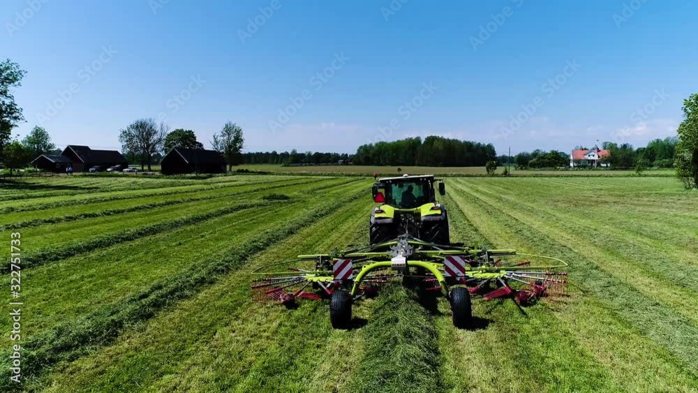 Drone aerial shot following a green tractor straight collecting grass on a Swedish summers field with sunny blue skies then tilting the camera down and flying above it.