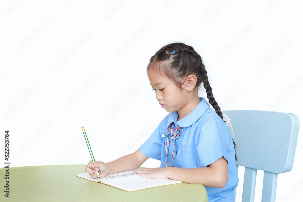 Intend little kid girl in school uniform writing on notebook at desk isolated over white background. Intend little kid girl in school uniform writing on notebook at desk isolated over white background.