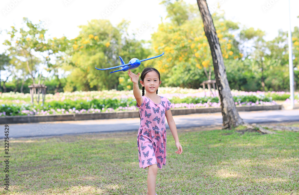 Cheerful little girl raise up a blue toy airplane flying on air in the garden outdoor.