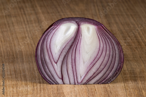 Red onion is cut in half and lies on a white oak kitchen board, with artificial lighting. Still life for the kitchen or element of the vegetarian menu.
