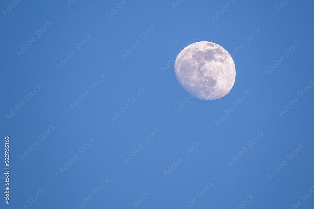 Almost full moon on a blue sky detailed during day time