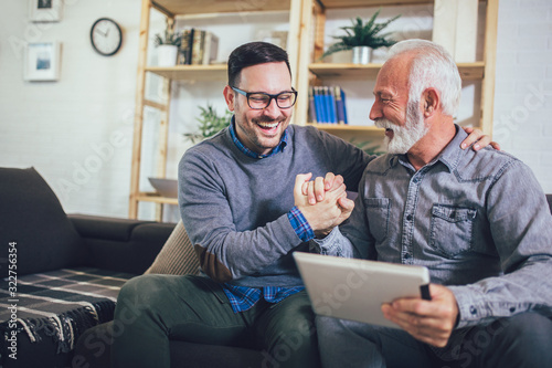 Portrait of senior man with adult son using digital tablet at home