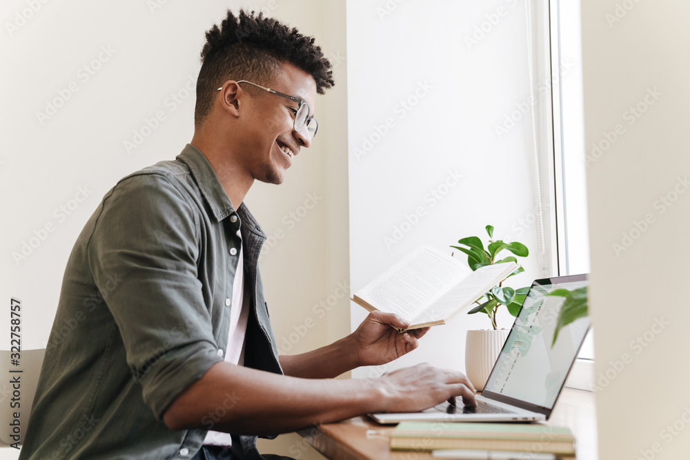 Fototapeta premium Positive smiling african guy using laptop computer.