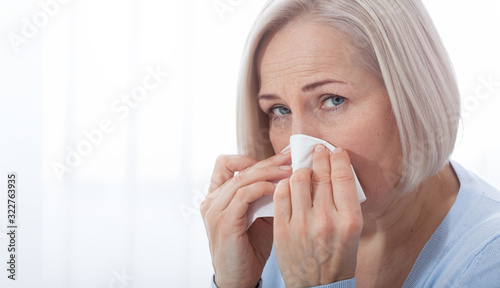 Healthcare, cold, allergy and people concept, sick woman blowing her runny nose in paper tissue on white background