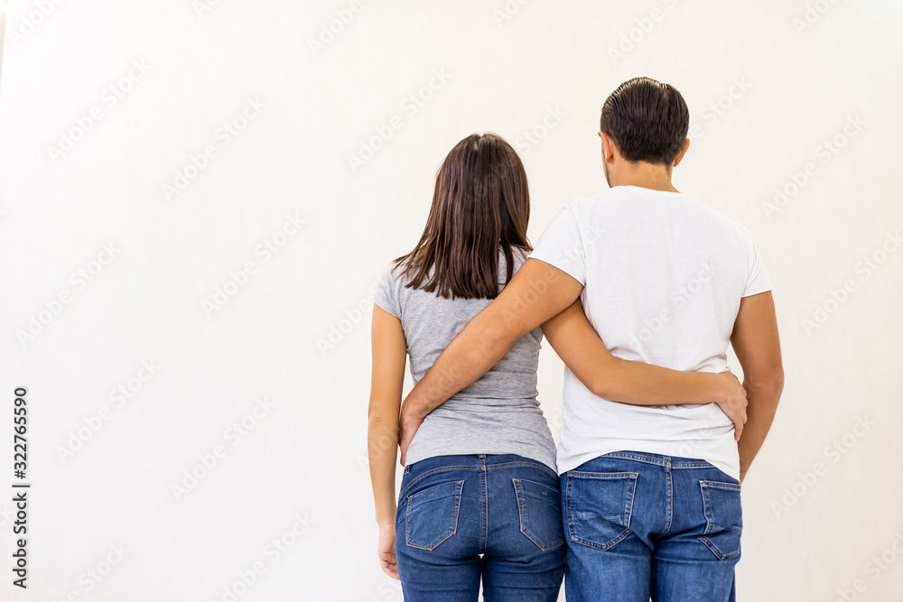 Back view of young couple standing together, embracing, looking at white wall.
