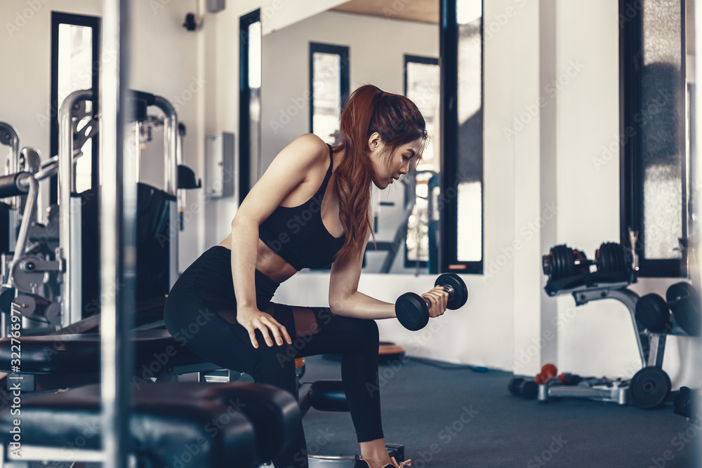 Sexy women lifting dumbbells workouts with dumbbells in a gym. Sport women at fitness.