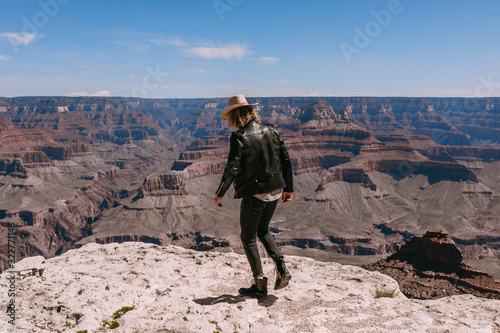 A Curly haired blonde man, wearing a black leather jacket ,black jeans, black shoes, beige linen shirt and matching cowboy hat, background vistas of the Grand Canyon © Georgi