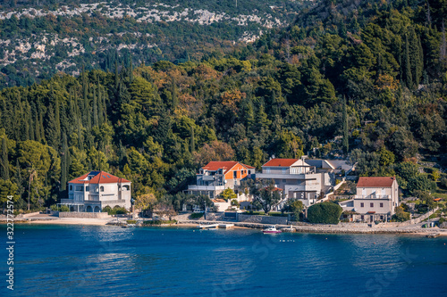 Panoramic landscape of mediterranean town on a sandy seacoast, deep blue sea on foreground, small houses with red tiled roofs situated on the shore, hills on background
