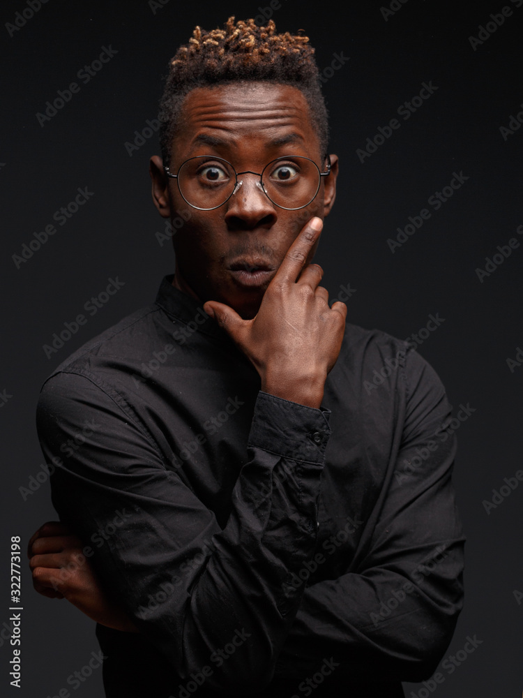 Fototapeta premium Emotional portrait of a young African man in black clothing against a dark background. Studio photography.