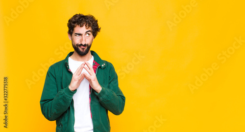 young crazy bearded man scheming and conspiring, thinking devious tricks and cheats, cunning and betraying against flat wall photo