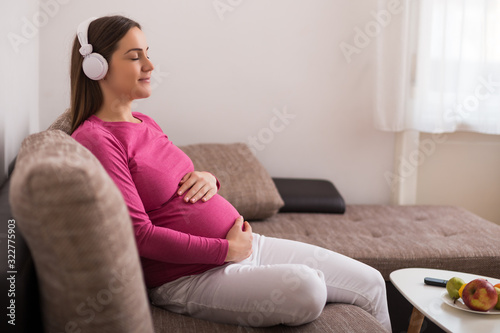Beautiful pregnant woman enjoys listening music at her home.