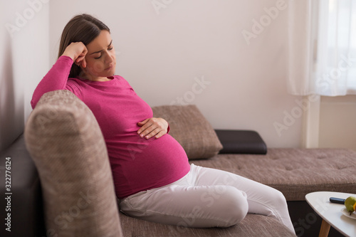 Sad pregnant woman tired of pregnancy is sitting on sofa at her home.