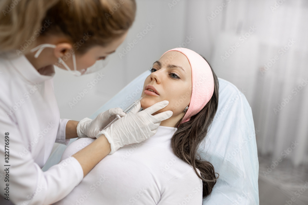 Permanent makeup, tattooing of lips. Cosmetologist in white gloves applying make up for woman in beauty salon