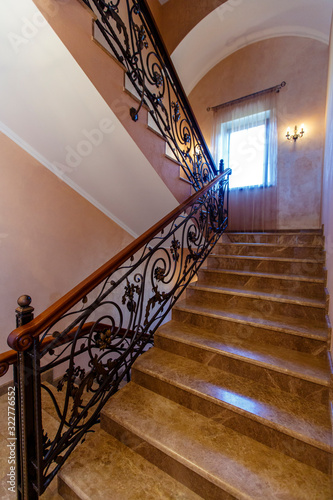 Stairs in the cottage with wrought iron railings and wooden handrails. Marble steps.