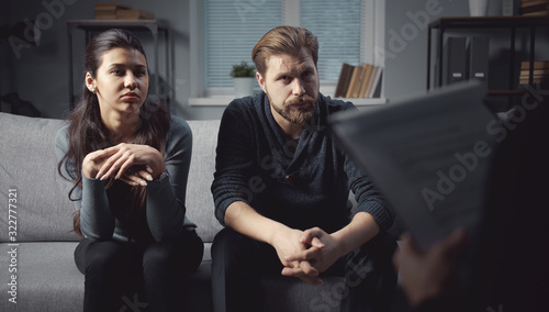 Fototapeta Naklejka Na Ścianę i Meble -  Attentive couple sitting on couch leaning forward listening to psychologue giving advice