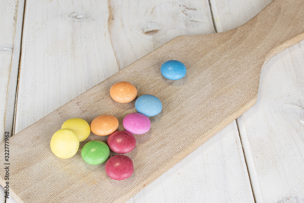 Group of ten whole sweet colourful candy on wooden cutting board on white wood Group of ten whole sweet colourful candy on wooden cutting board on white wood