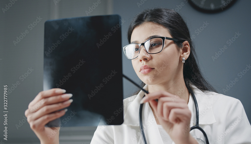 Portrait of young nice woman doctor wearing eyeglasses stethoscope watching patient's x-ray image Portrait of young nice woman doctor wearing eyeglasses stethoscope watching patient's x-ray image