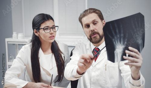 Two doctors discussing patient's hands xray image, preceptor showing roentgenogram details to intern