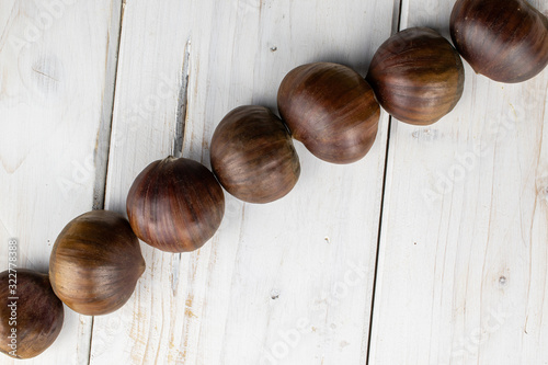 Group of seven whole edible brown chestnut diagonal flatlay on white wood photo